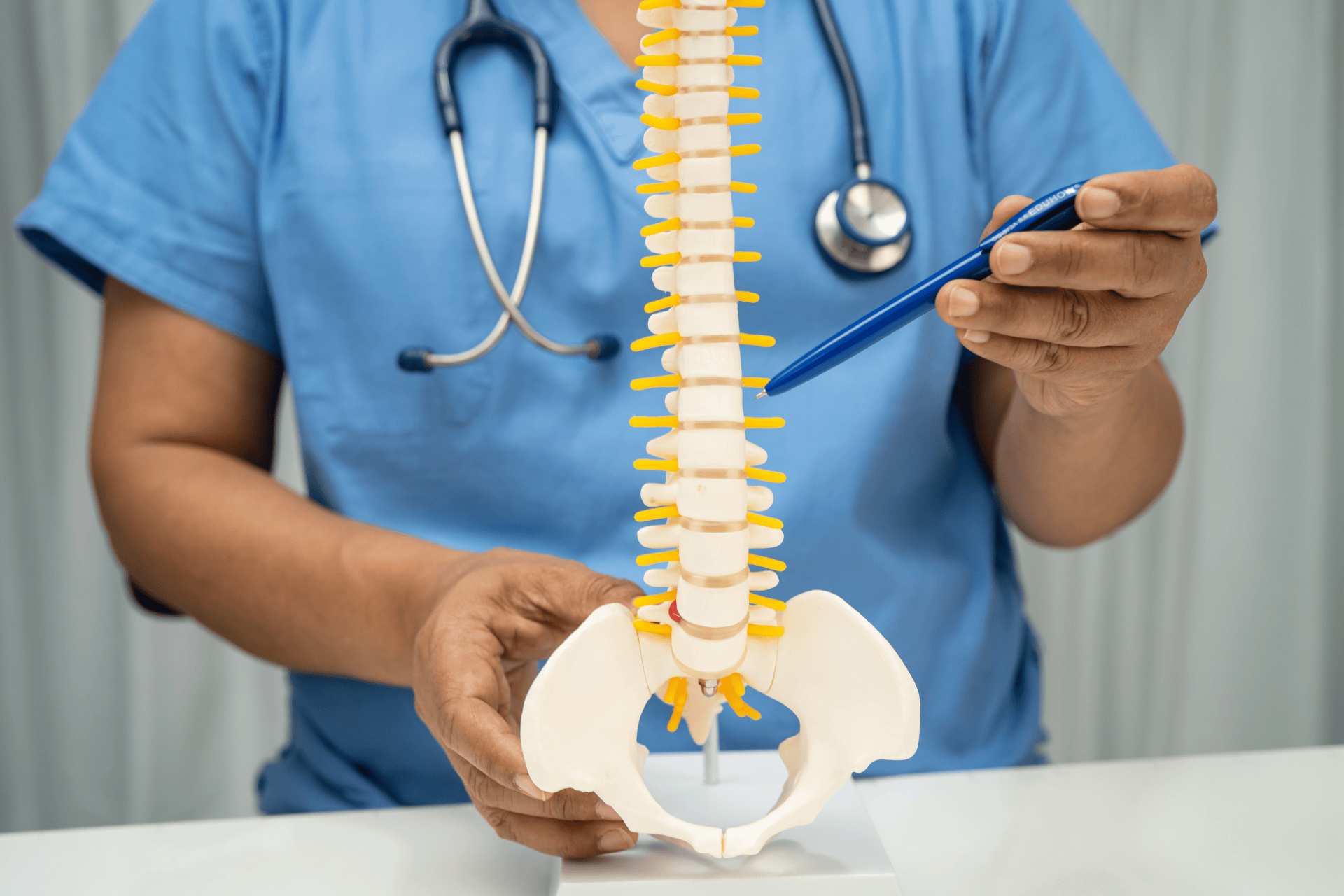 A healthcare professional points to a spine model with a pen, illustrating lumbar spondylosis in the lower back.