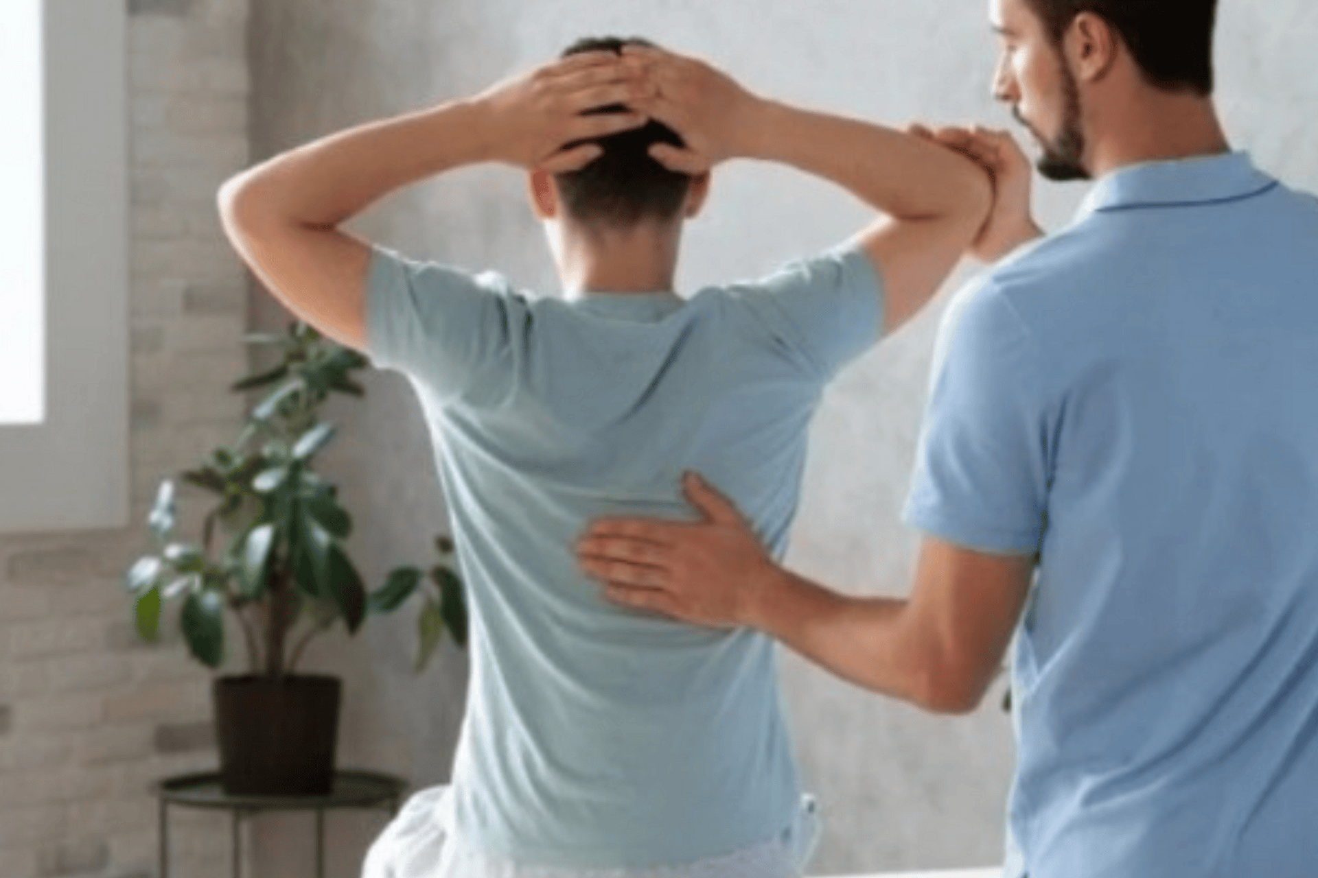 A man with sciatica stands with his hands behind his head while a chiropractor places a hand on his lower back during treatment.