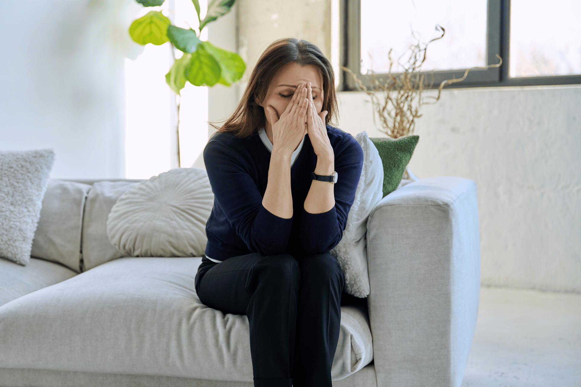 Woman sitting on a couch with her face in her hands, appearing exhausted, symbolizing perimenopause fatigue.