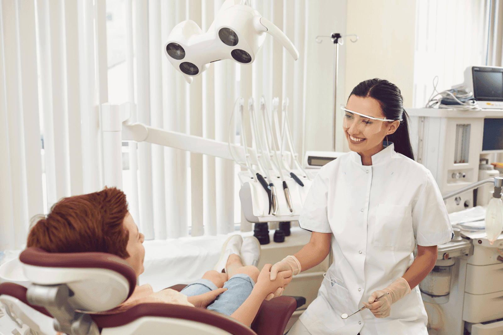 Dentist smiling and holding a patient’s hand during a dental checkup