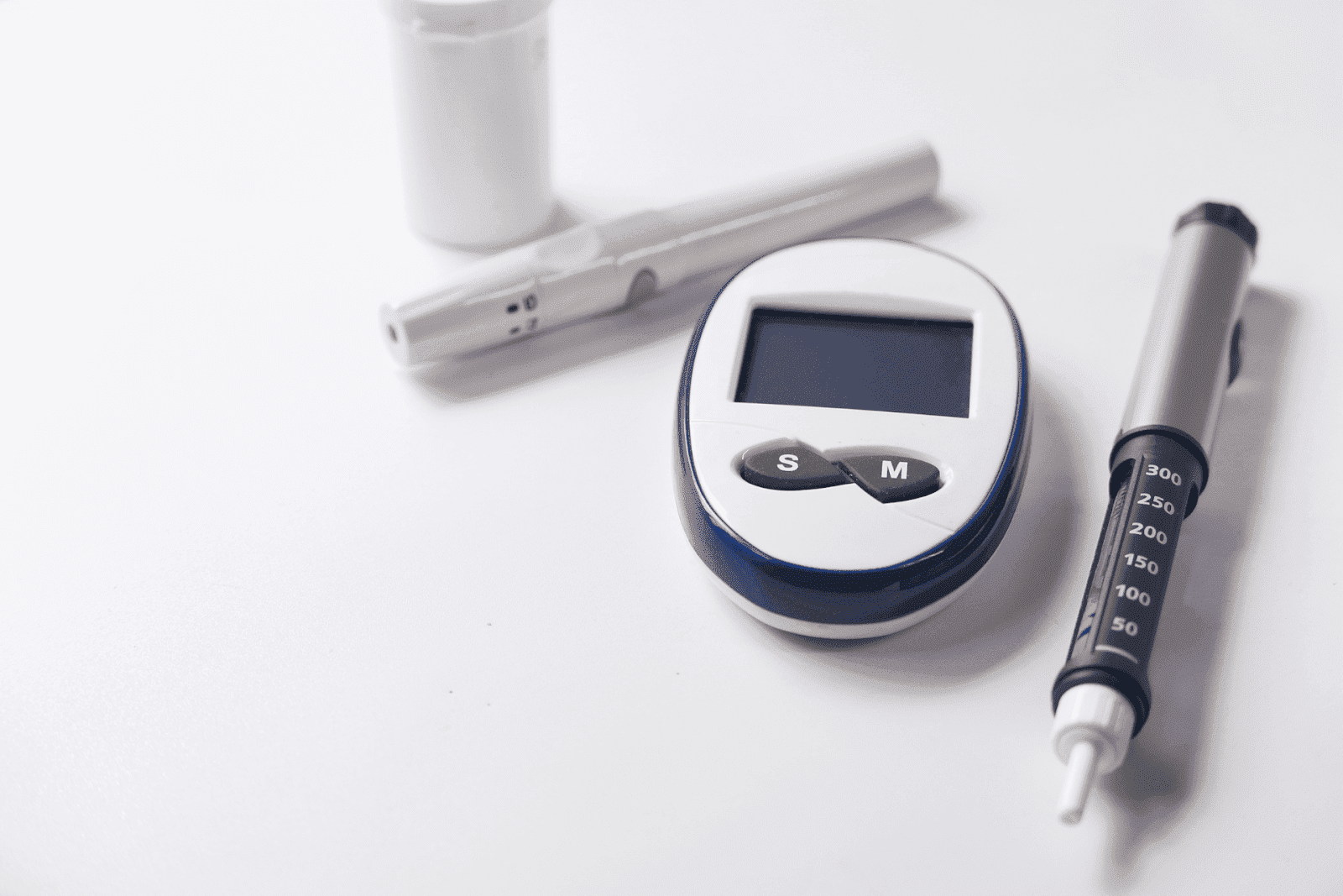 Diabetes management tools, including a glucose meter, lancet device, and insulin pen on a white surface