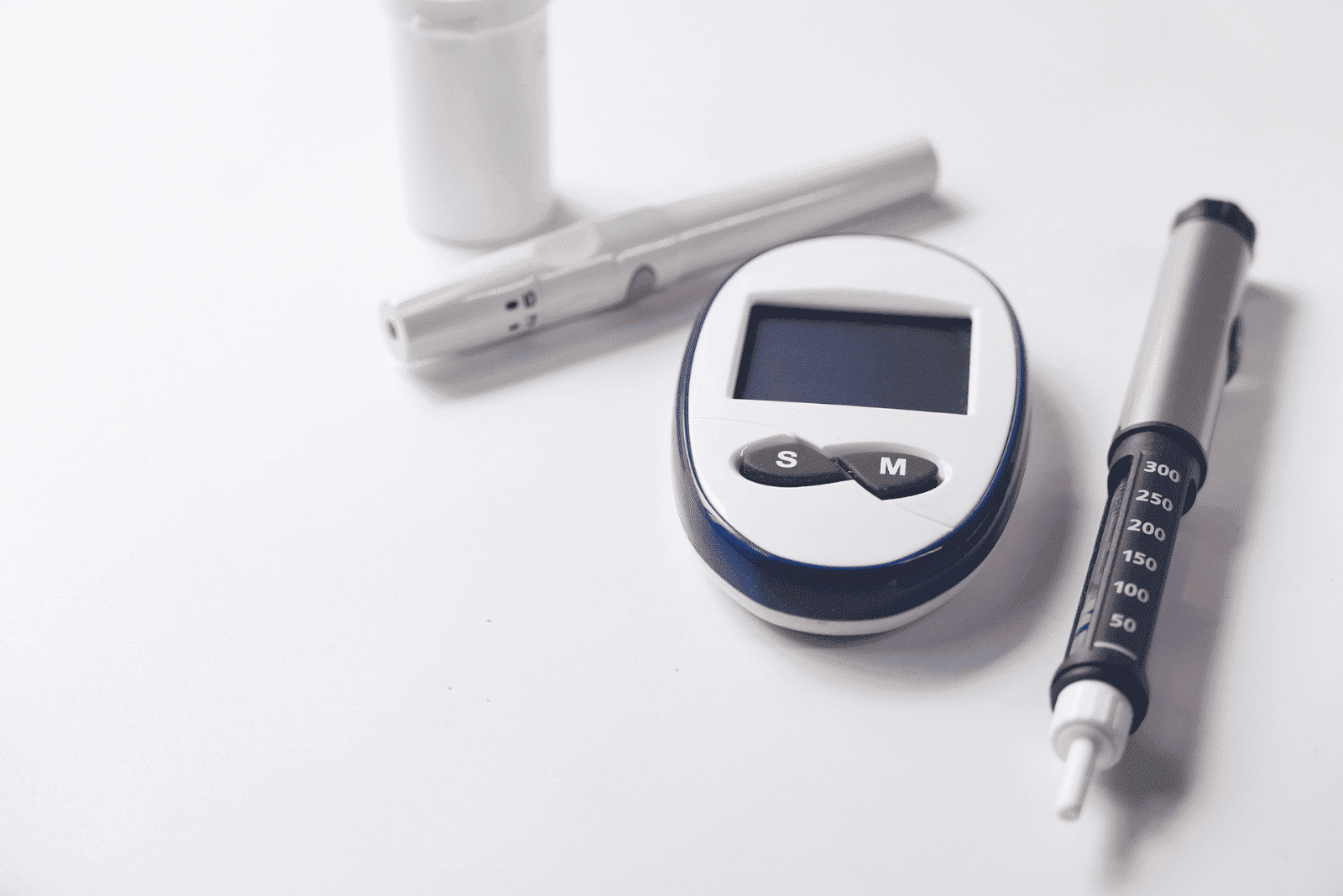 Diabetes monitoring tools, including a glucose meter, insulin pen, and lancing device, on a white surface.