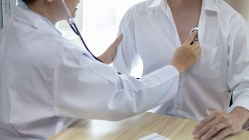 Doctor checking heart beat of male patient.
