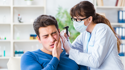 Doctor checking ear of man holding face in pain