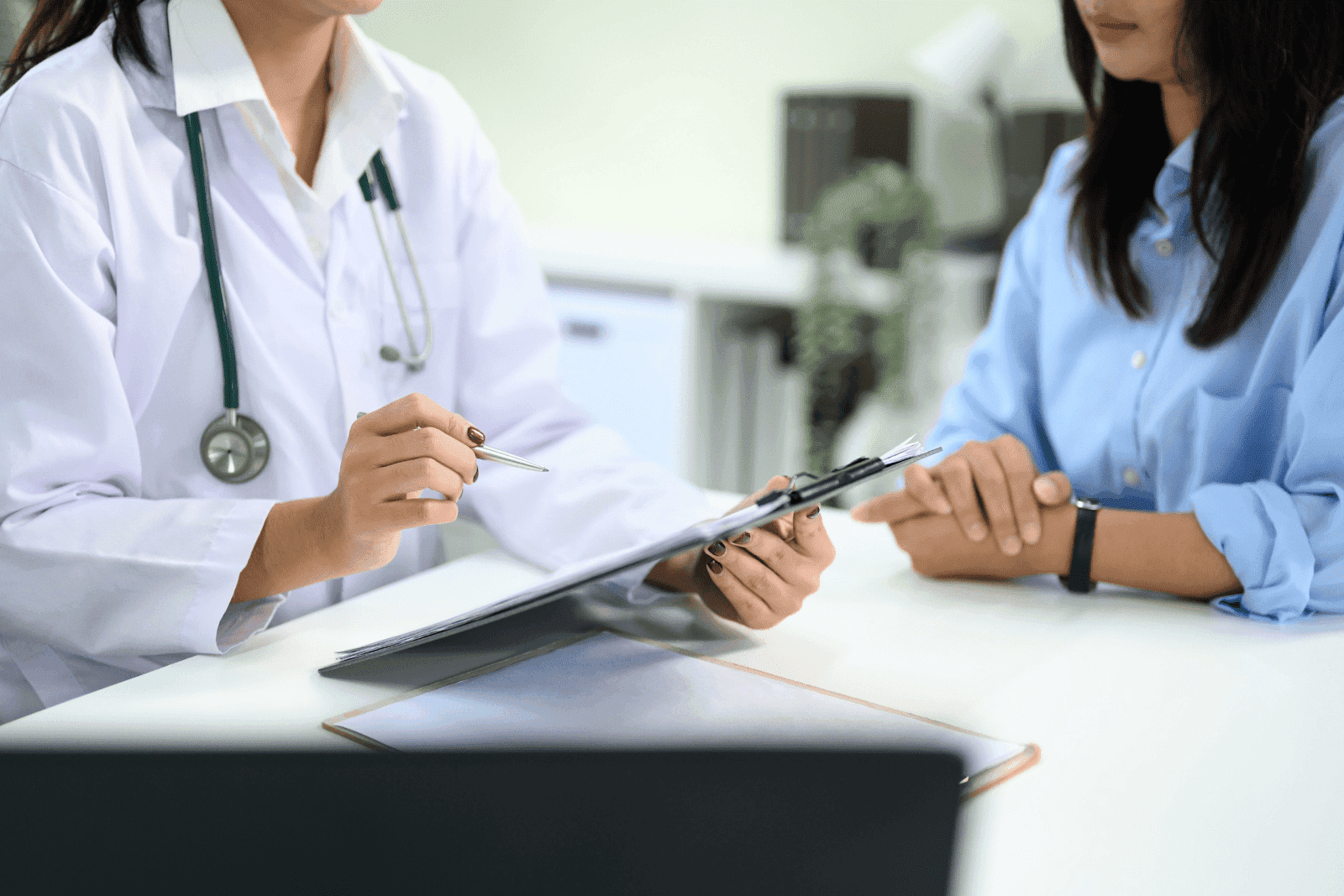Doctor discussing medical notes with a patient at a desk.