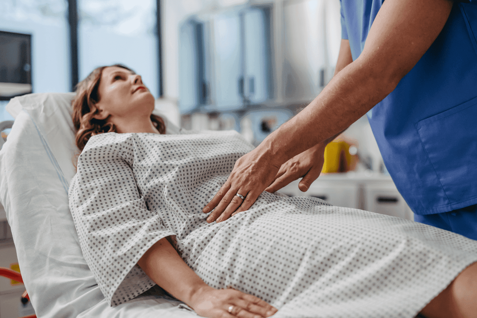 Doctor examining a female patient’s abdomen in a hospital bed.