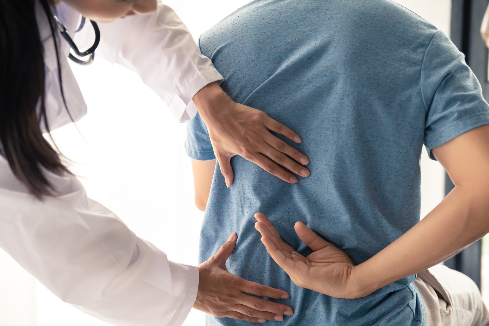 Doctor examining a patient’s back while the patient holds their lower back