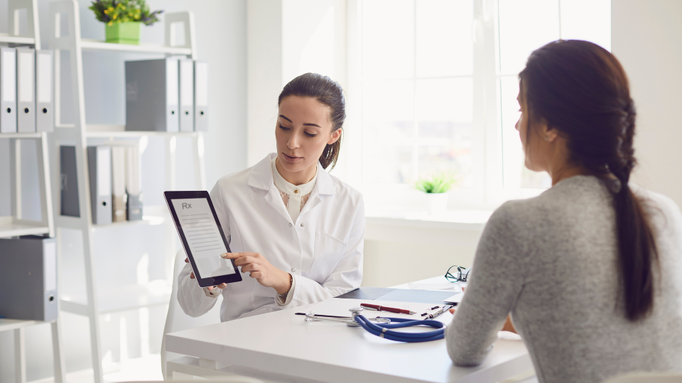 A doctor showing a digital prescription on a tablet to a patient across the desk.
