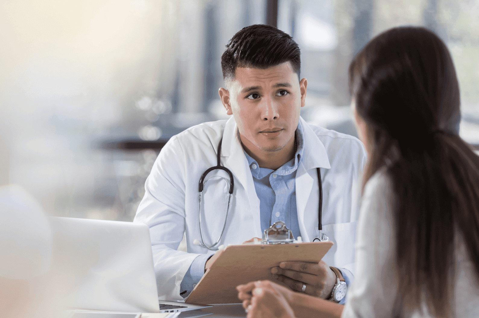 Doctor holding a clipboard and talking with a patient during a consultation.