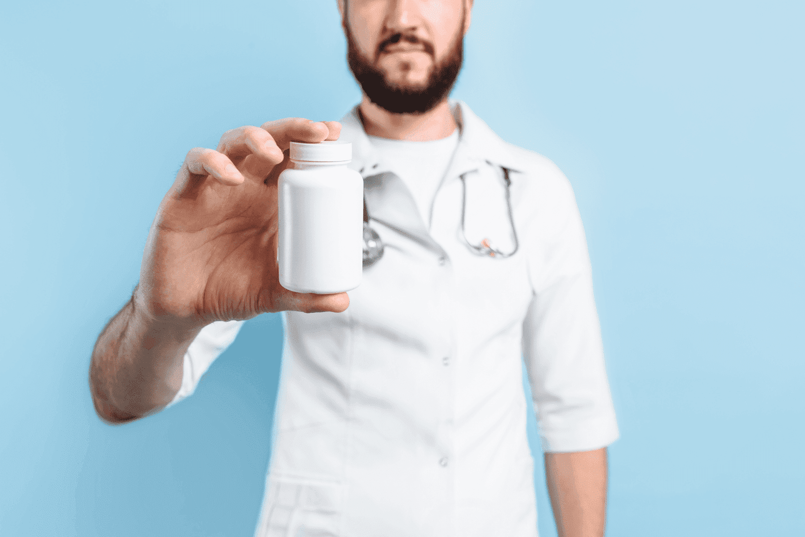 Doctor holding a white pill bottle in hand against a blue background.