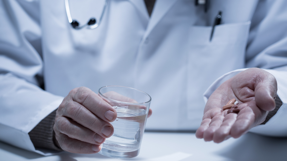 Doctor holding glass of water in one hand and pills in the other hand.