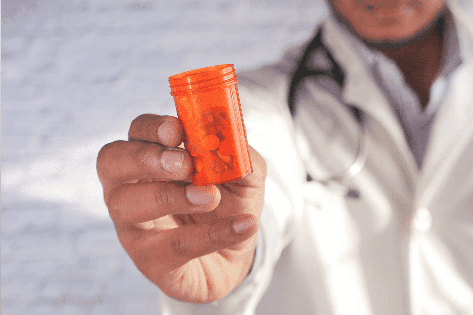 Doctor holding up an orange pill bottle filled with tablets toward the camera.