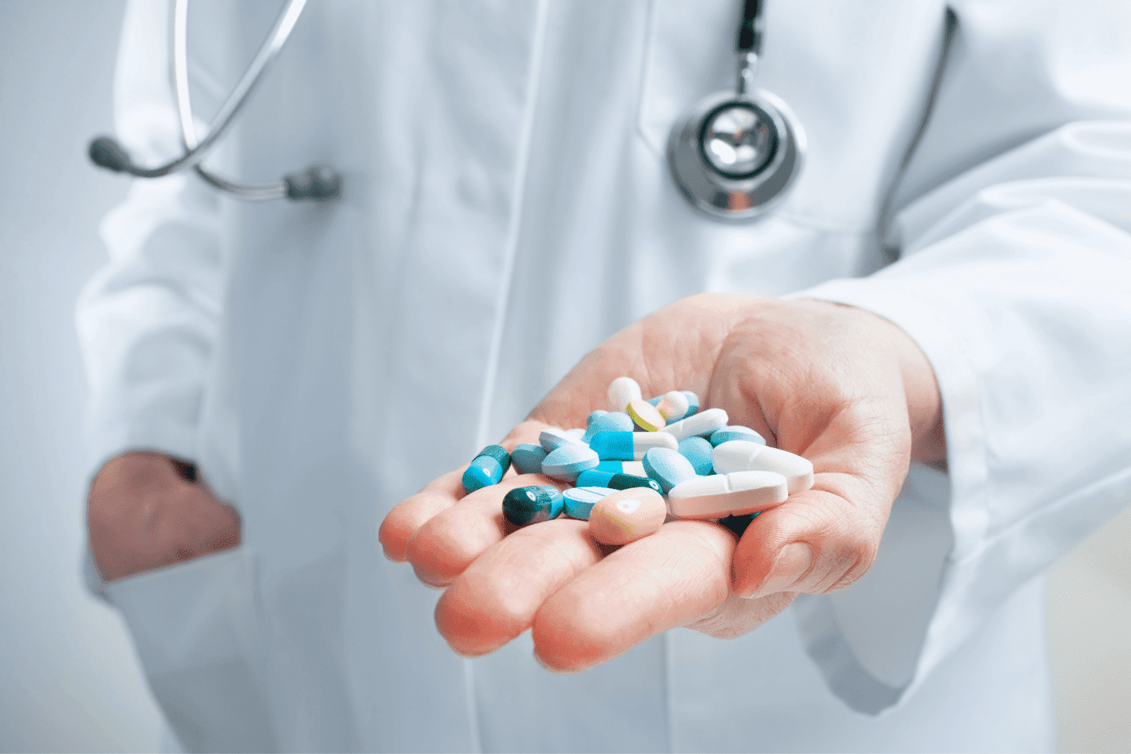 Doctor in a white coat holding a handful of assorted pills.