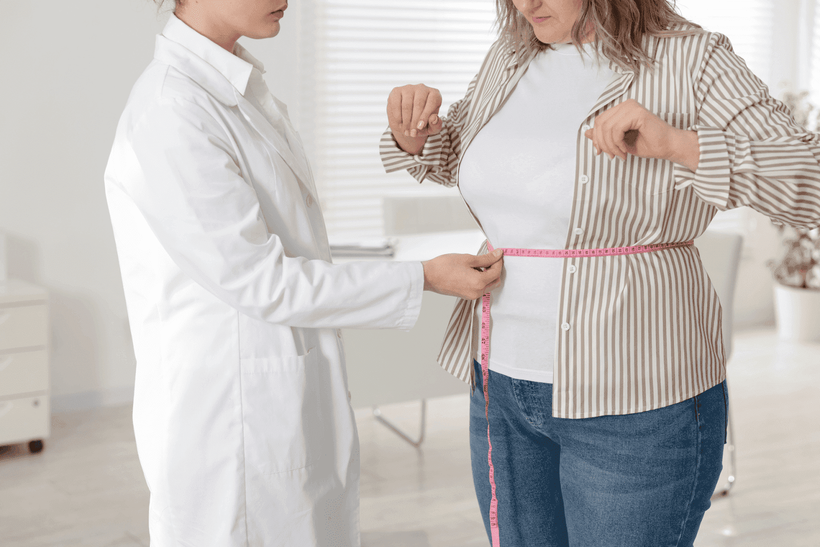 Doctor measuring a patient’s waist with a pink tape measure