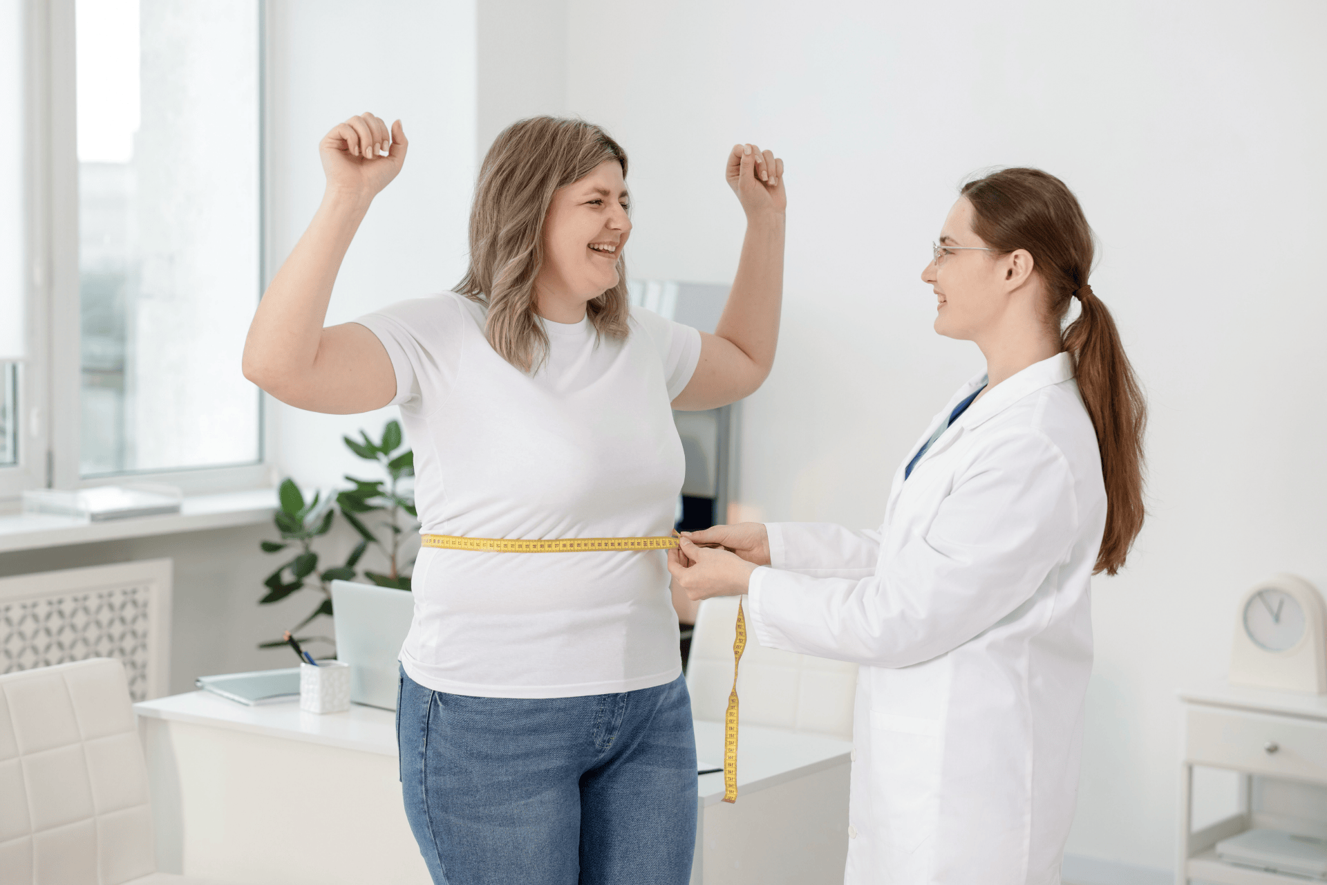 Doctor measuring a woman’s waist with a tape measure while she celebrates progress.