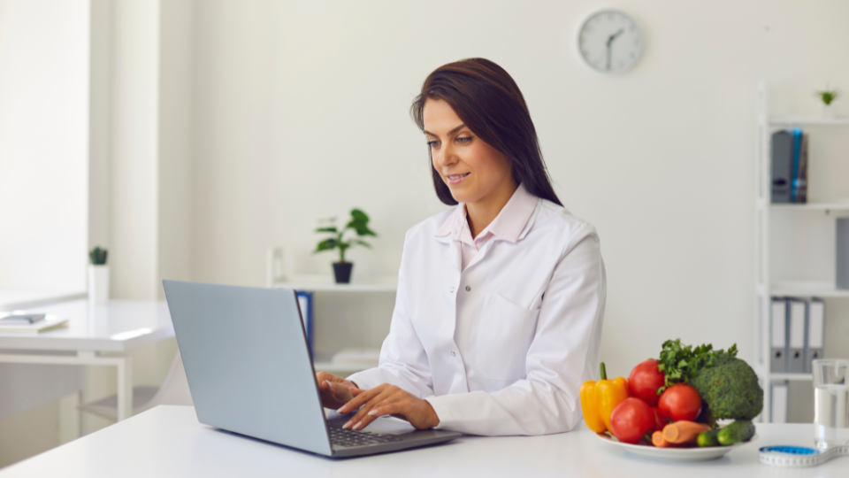 Doctor using laptop with plate of veggies on the table
