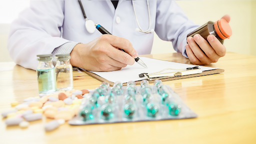Doctor writing prescription with different medicines and pills on table