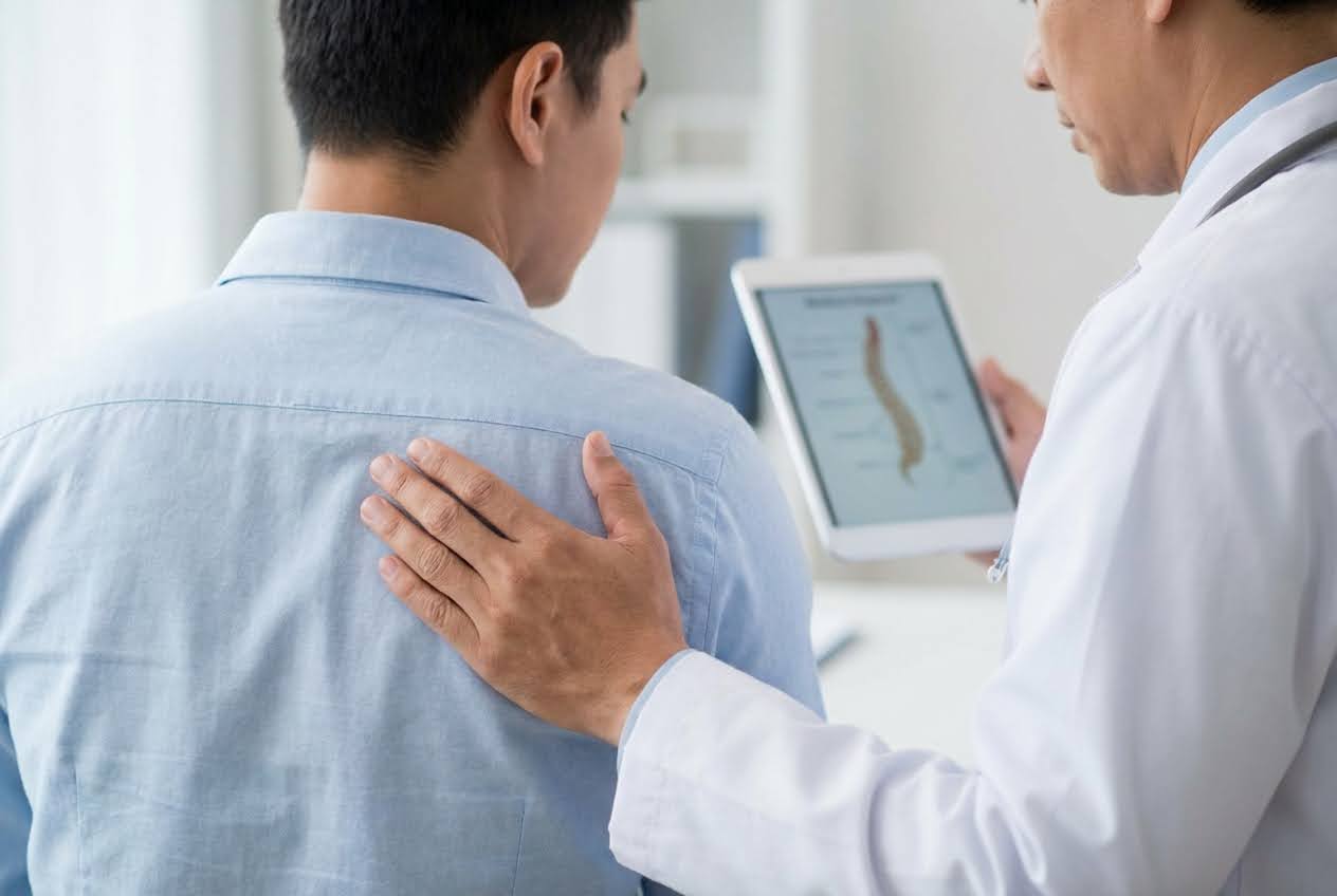 Doctor's hand on a patient's back, while holding a tablet displaying a spine diagram.