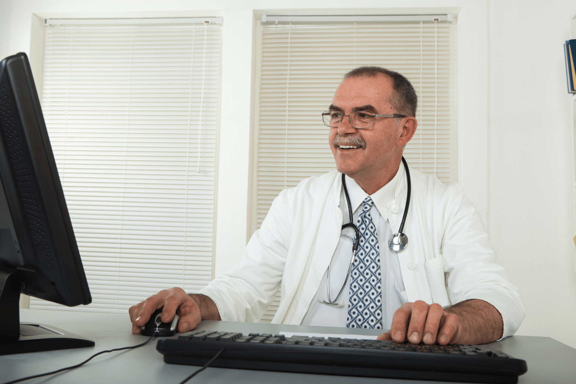 Doctor sitting at a desk using a computer and smiling.