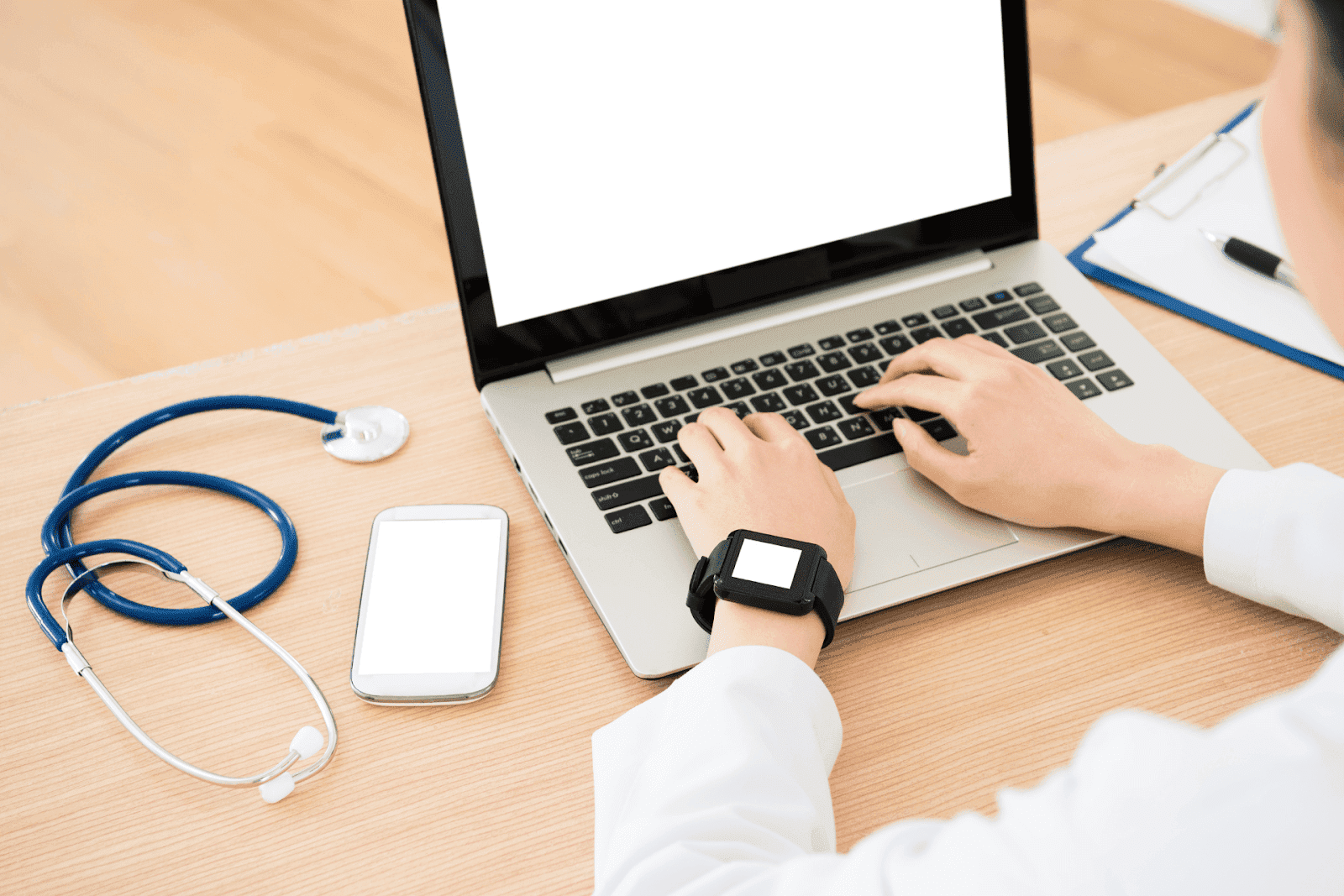 Doctor typing on laptop with stethoscope, phone, and smartwatch