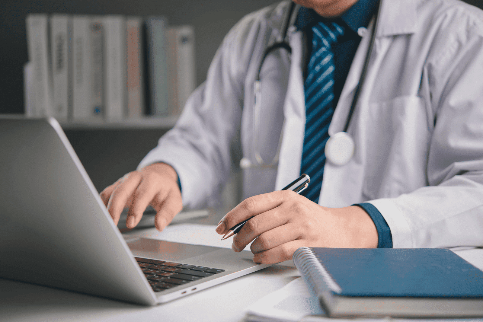 Doctor using a laptop and writing notes at a desk.