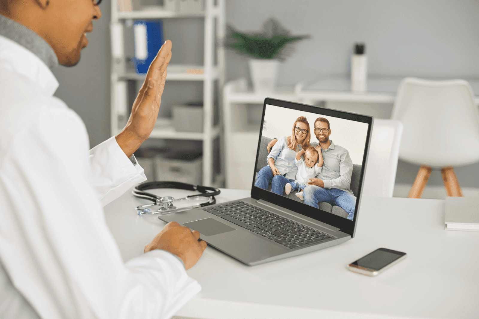 Doctor waving during an online video call with a family on a laptop screen.