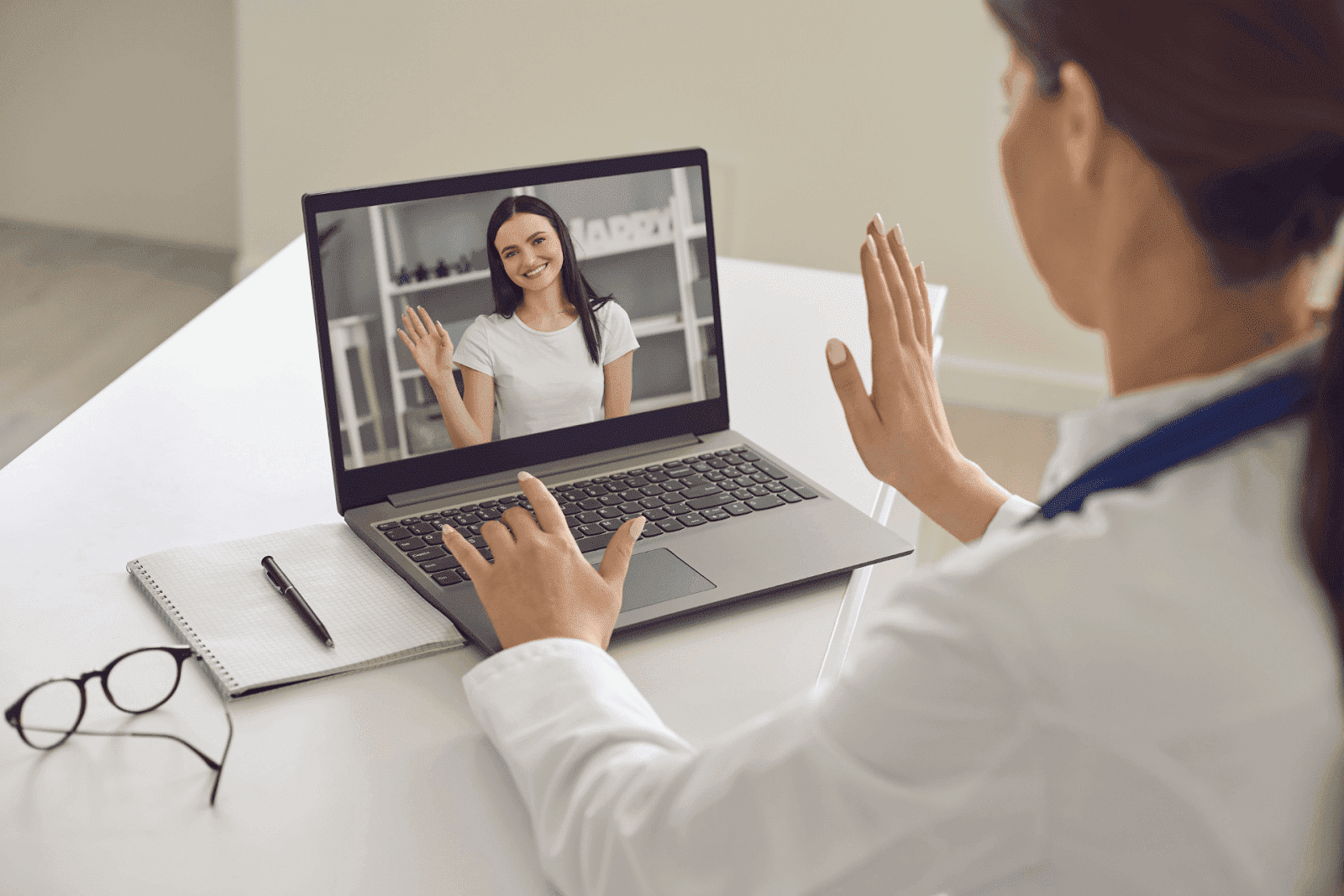 Doctor waving to a patient during a video call on a laptop