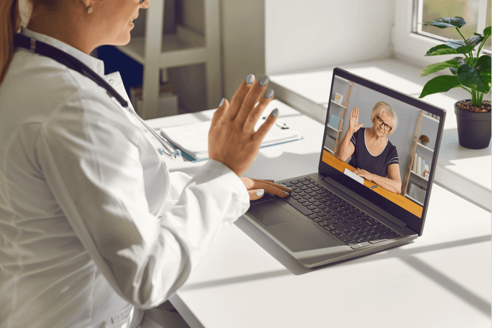 Doctor waving to an older woman during an online video consultation.