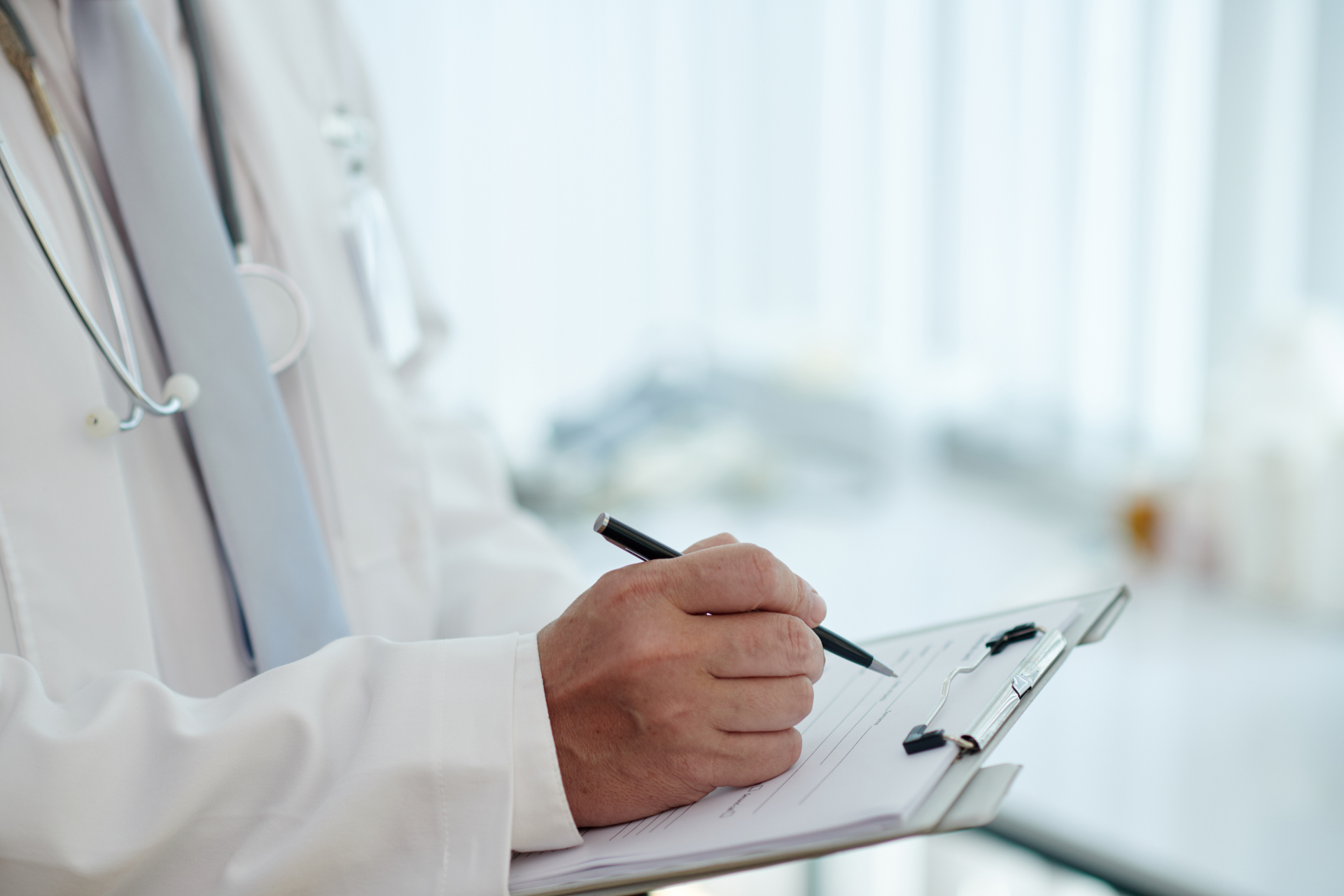 A doctor in a white coat writing on a clipboard with a stethoscope visible