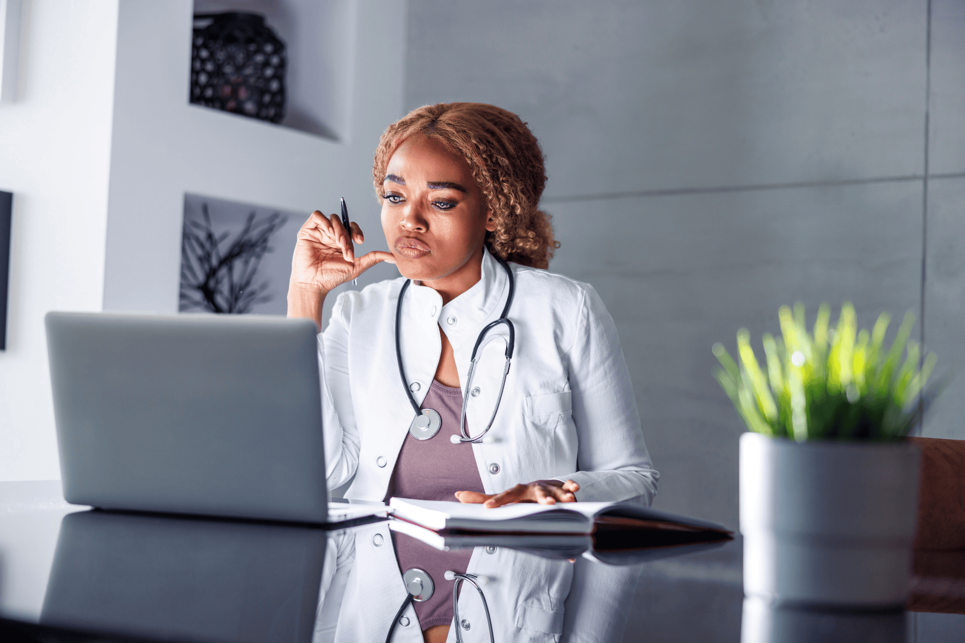 Doctor working at a desk, looking at a laptop with a stethoscope around her neck