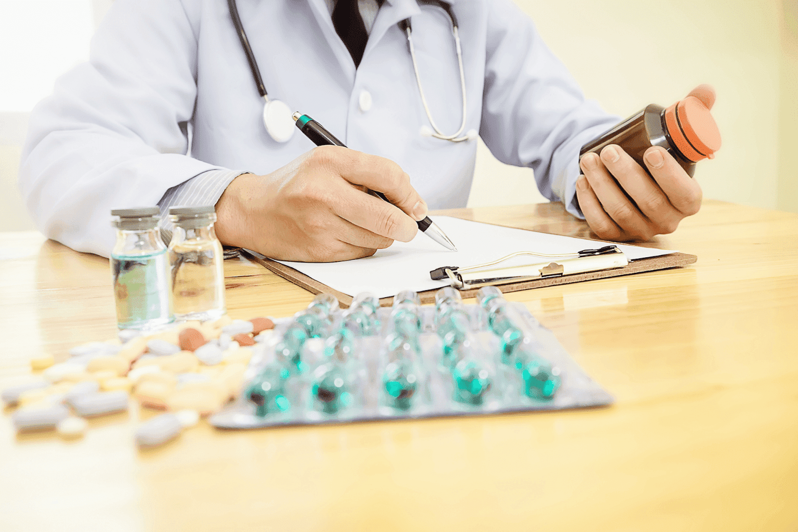 Doctor writing a prescription while holding a pill bottle with various medications on the table