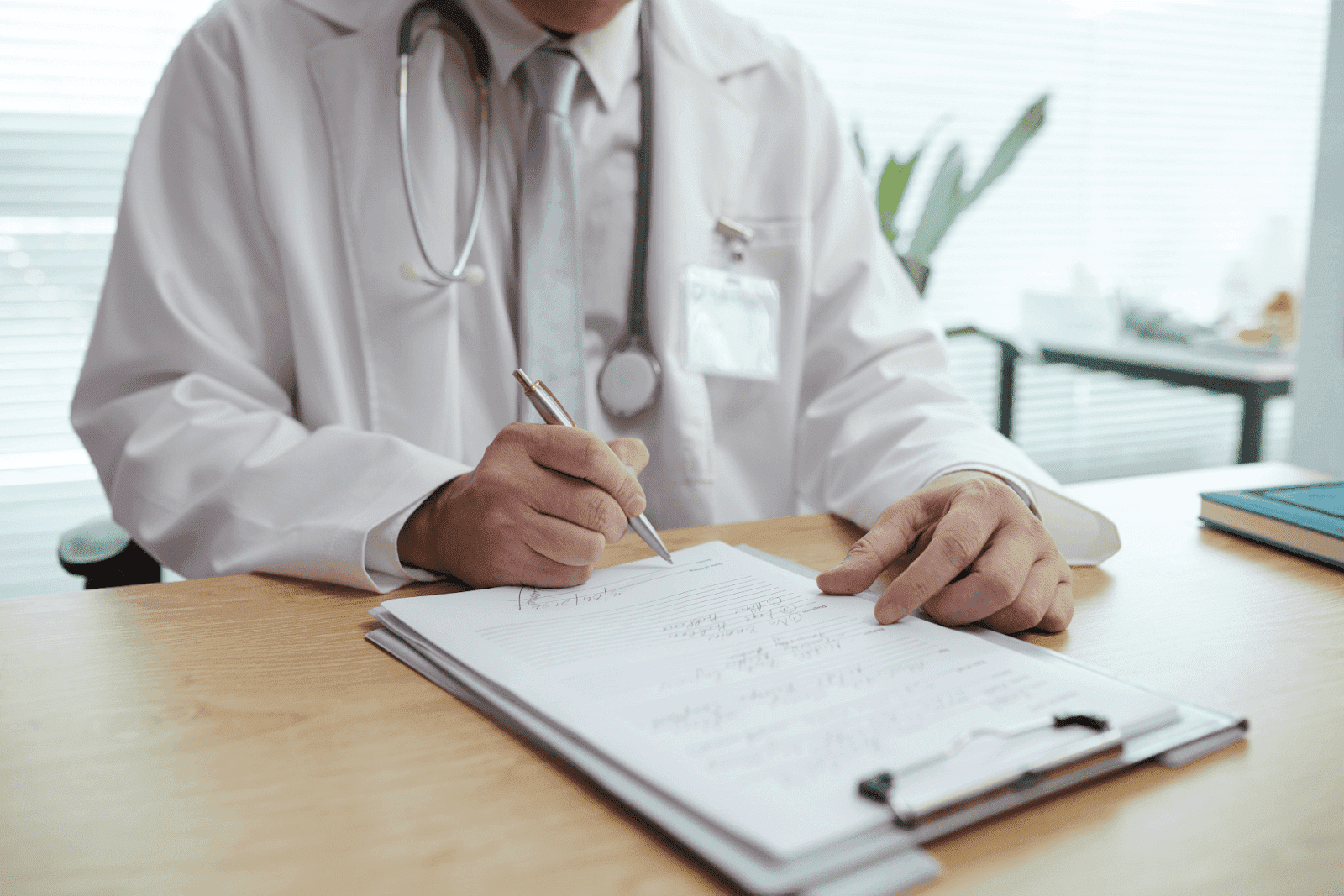 Doctor writing notes or a prescription on a clipboard at a desk.