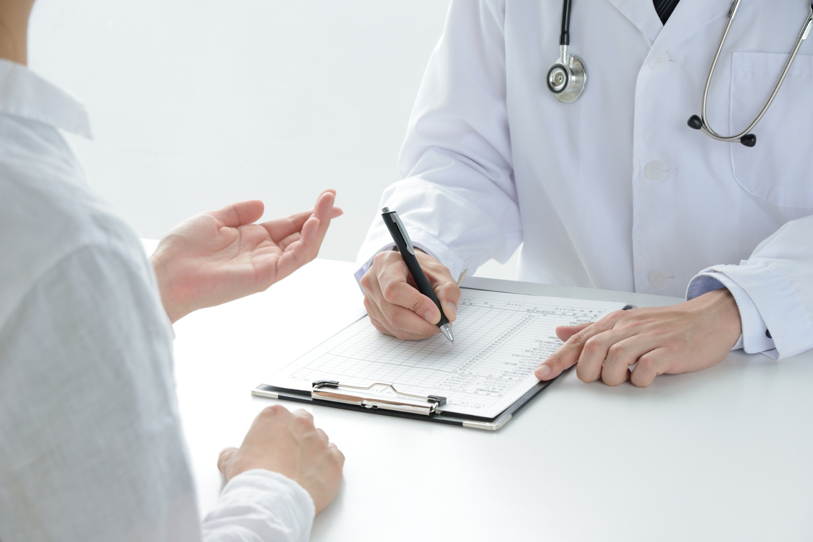 Doctor writing on a medical chart while speaking with a patient across the desk