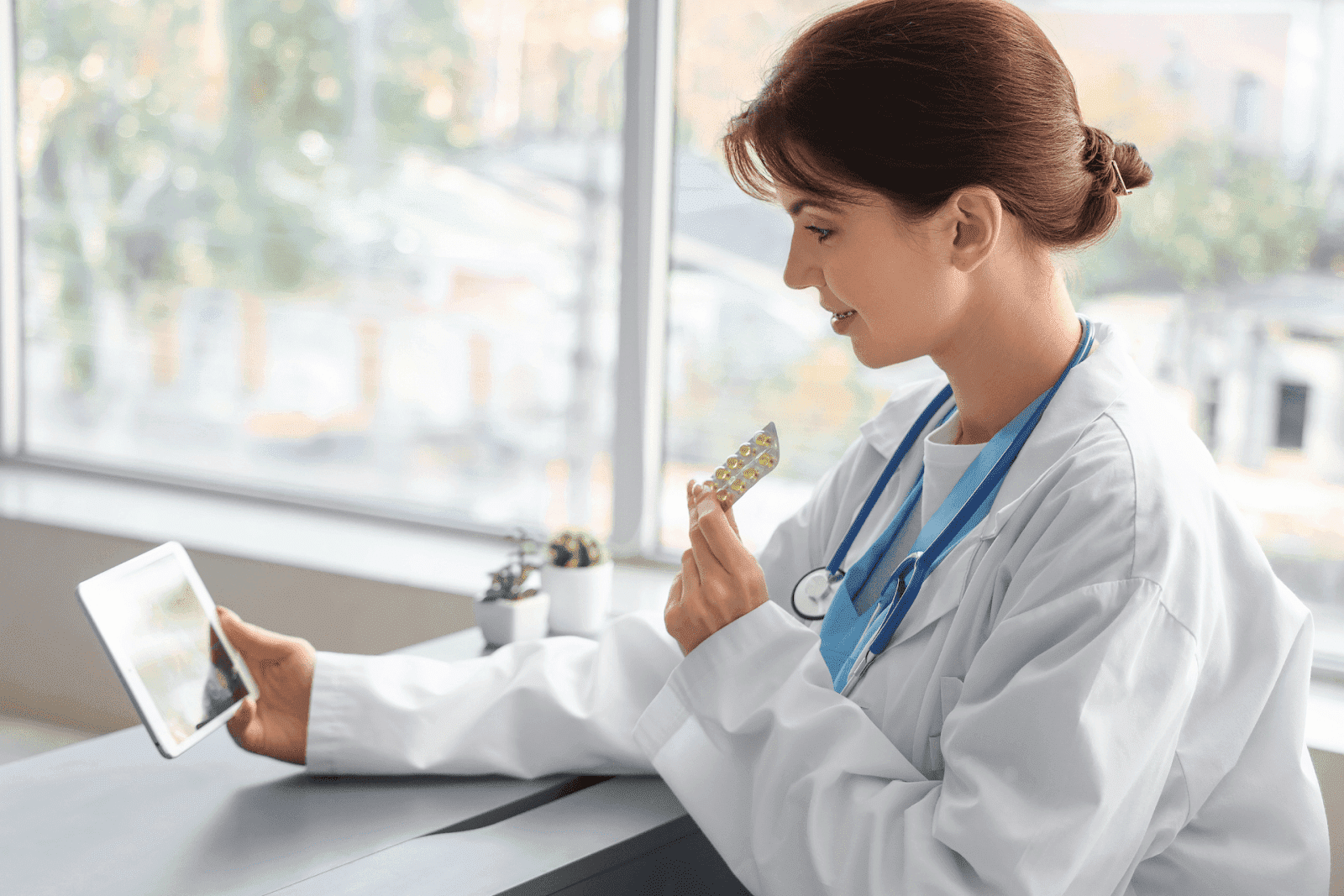 Female doctor holding a pill pack during an online consultation on a tablet.