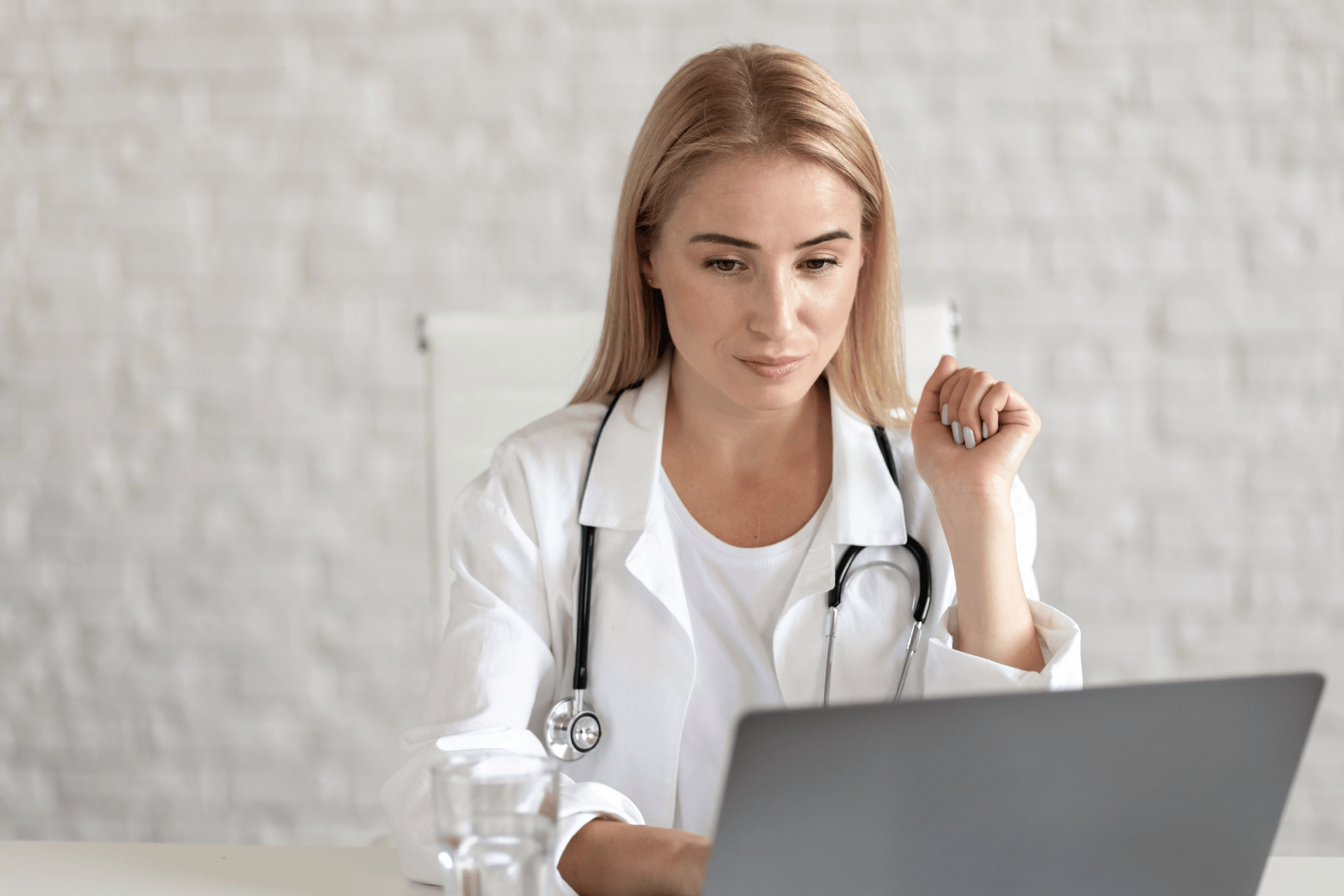 Female doctor in a white coat looking at a laptop during a virtual consultation