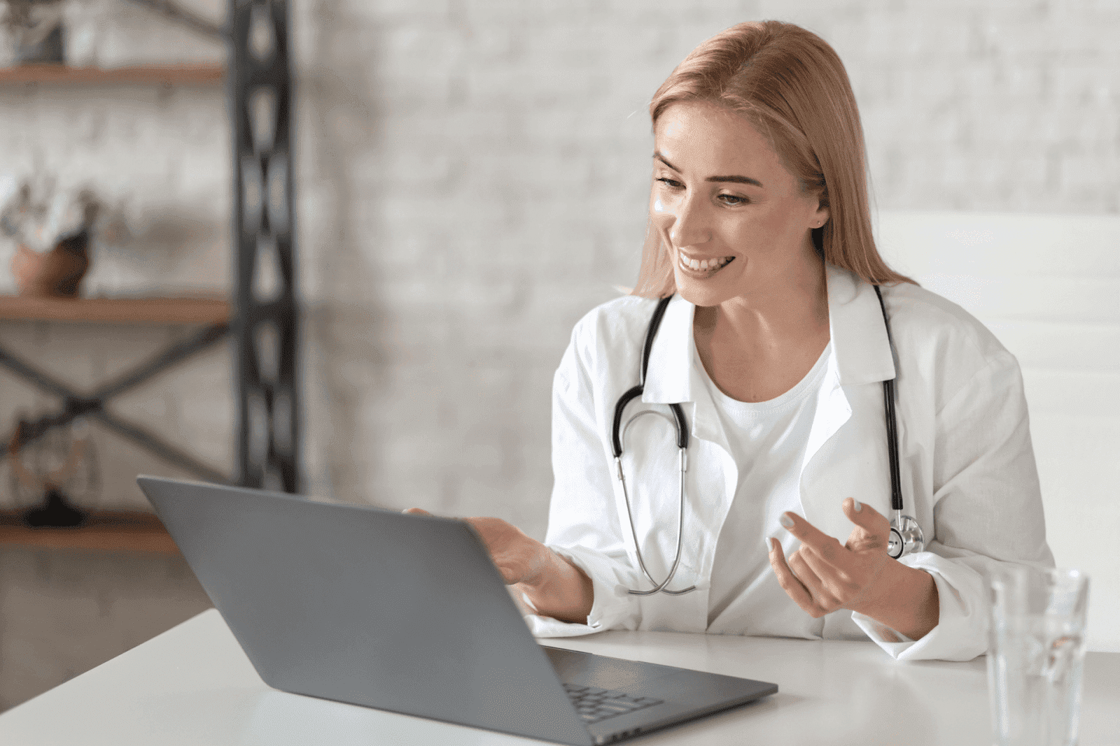 Female doctor smiling while talking to a patient online using a laptop