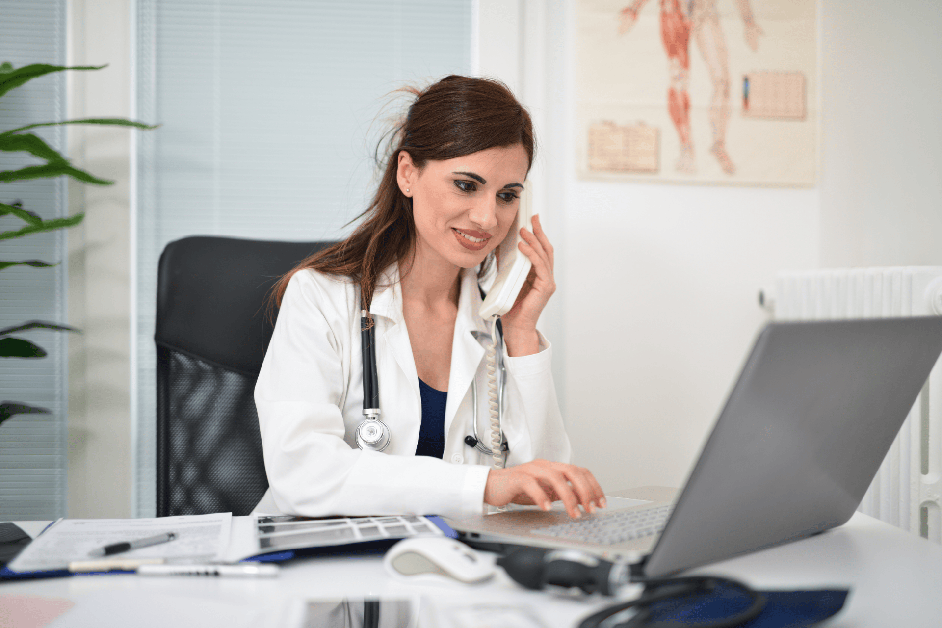 Female doctor talking on the phone while using a laptop.