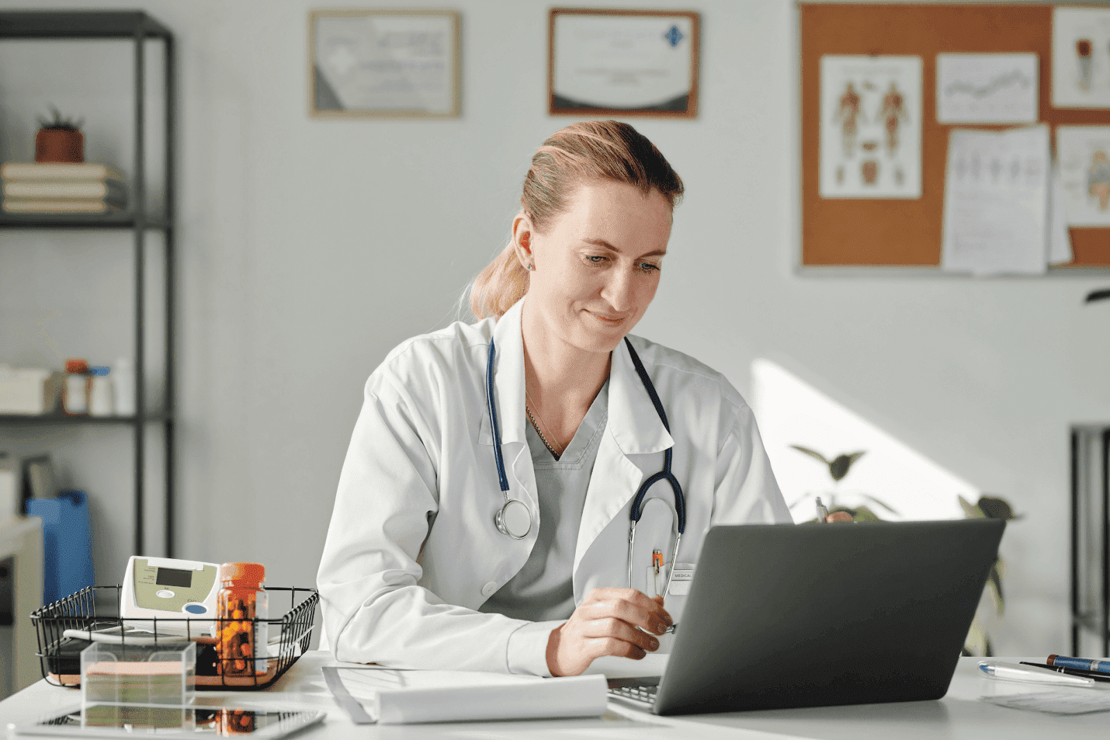 Female doctor working on a laptop in her office with medical tools on the desk.