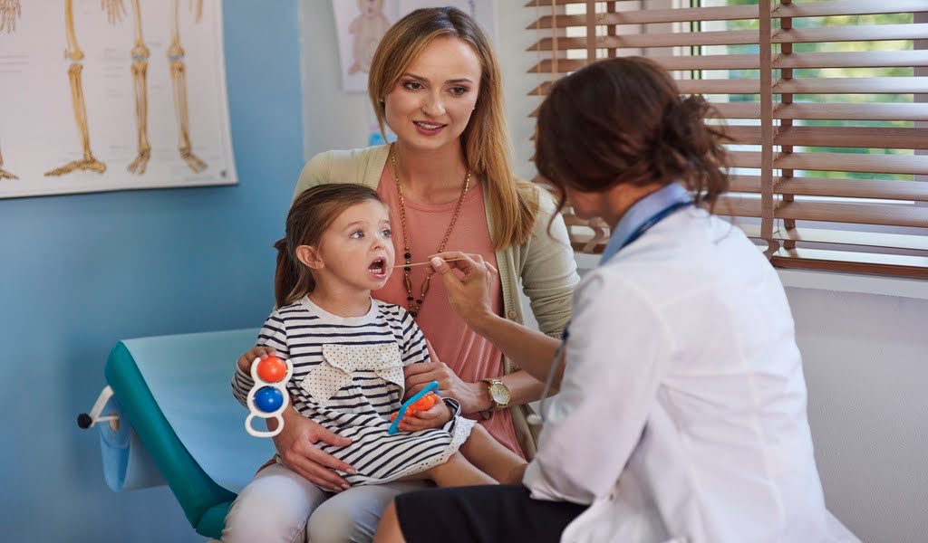A pediatrician examining a toddler while the mother observes