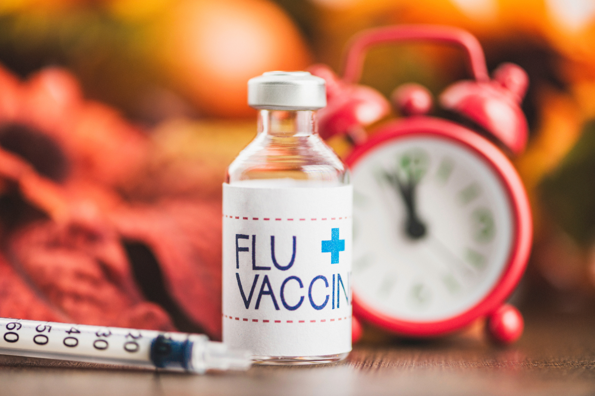 Flu vaccine vial with a syringe and an alarm clock in the background