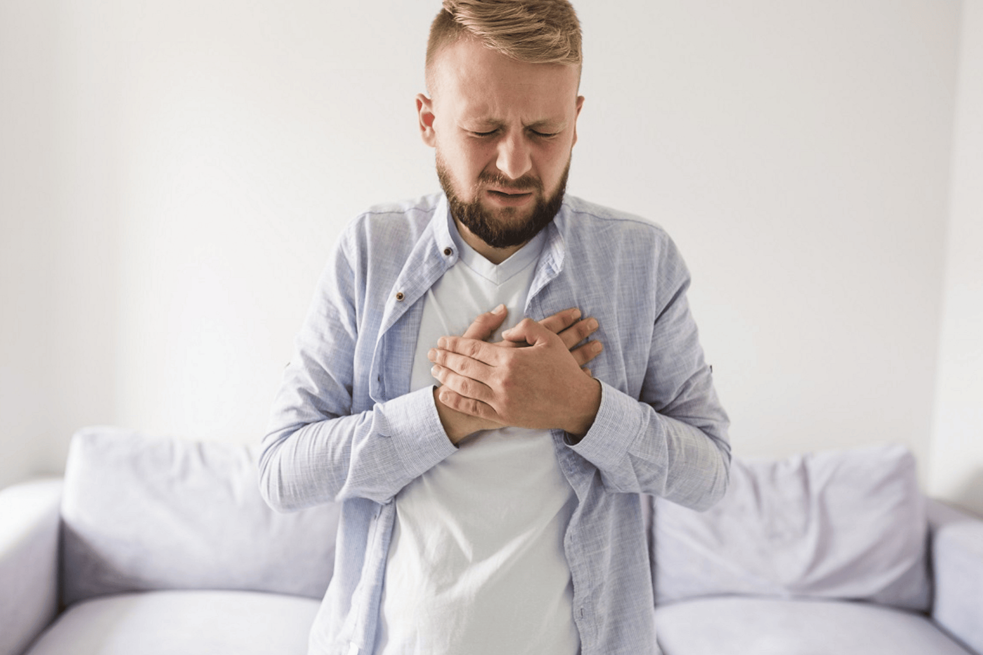 Man clutching his chest in pain while standing in a living room.