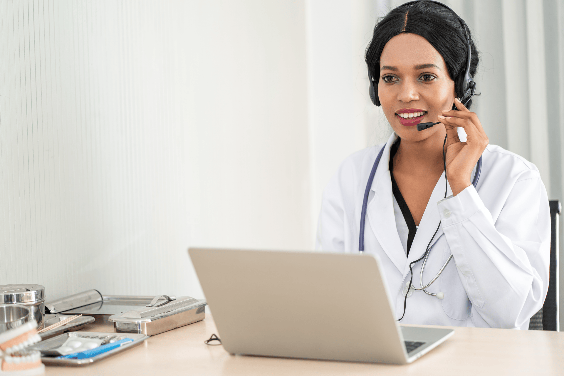 A doctor wearing a headset smiles while conducting an online consultation on a laptop