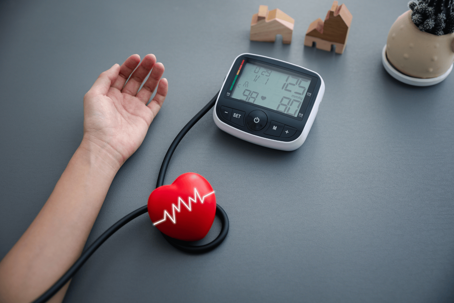 Person measuring blood pressure with a digital monitor and a red heart model nearby.