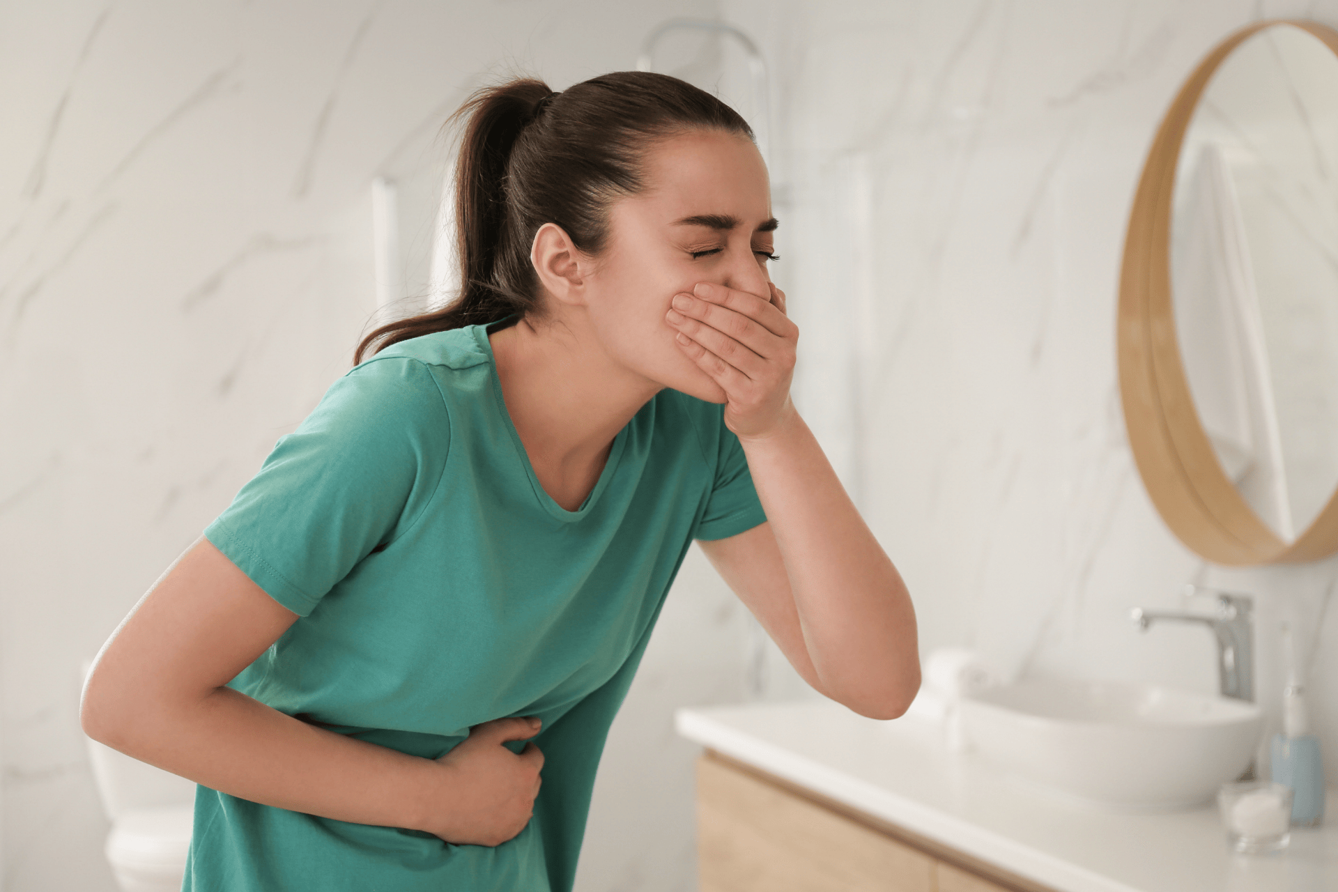 Woman in a bathroom feeling nauseous and holding her stomach.