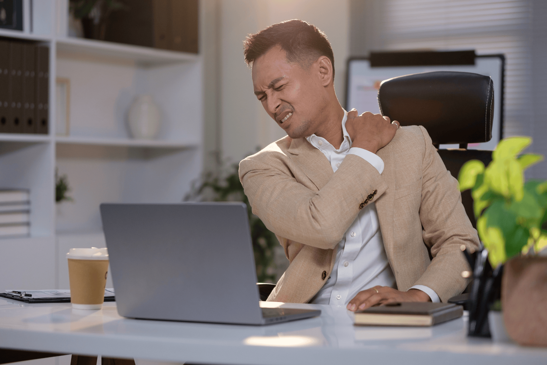 Man sitting at a desk, grimacing and holding his sore shoulder.