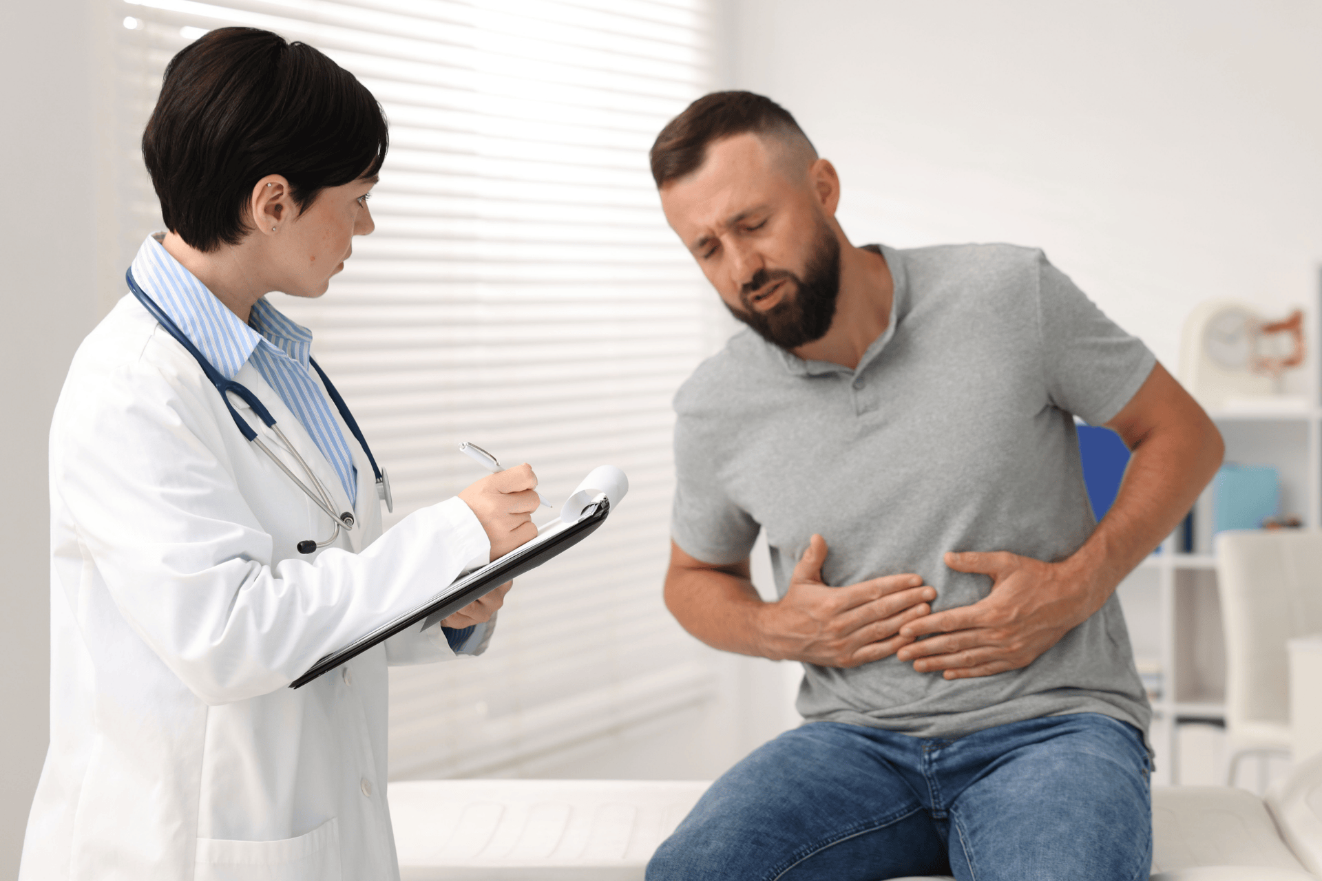 Doctor taking notes while examining a man with stomach pain.