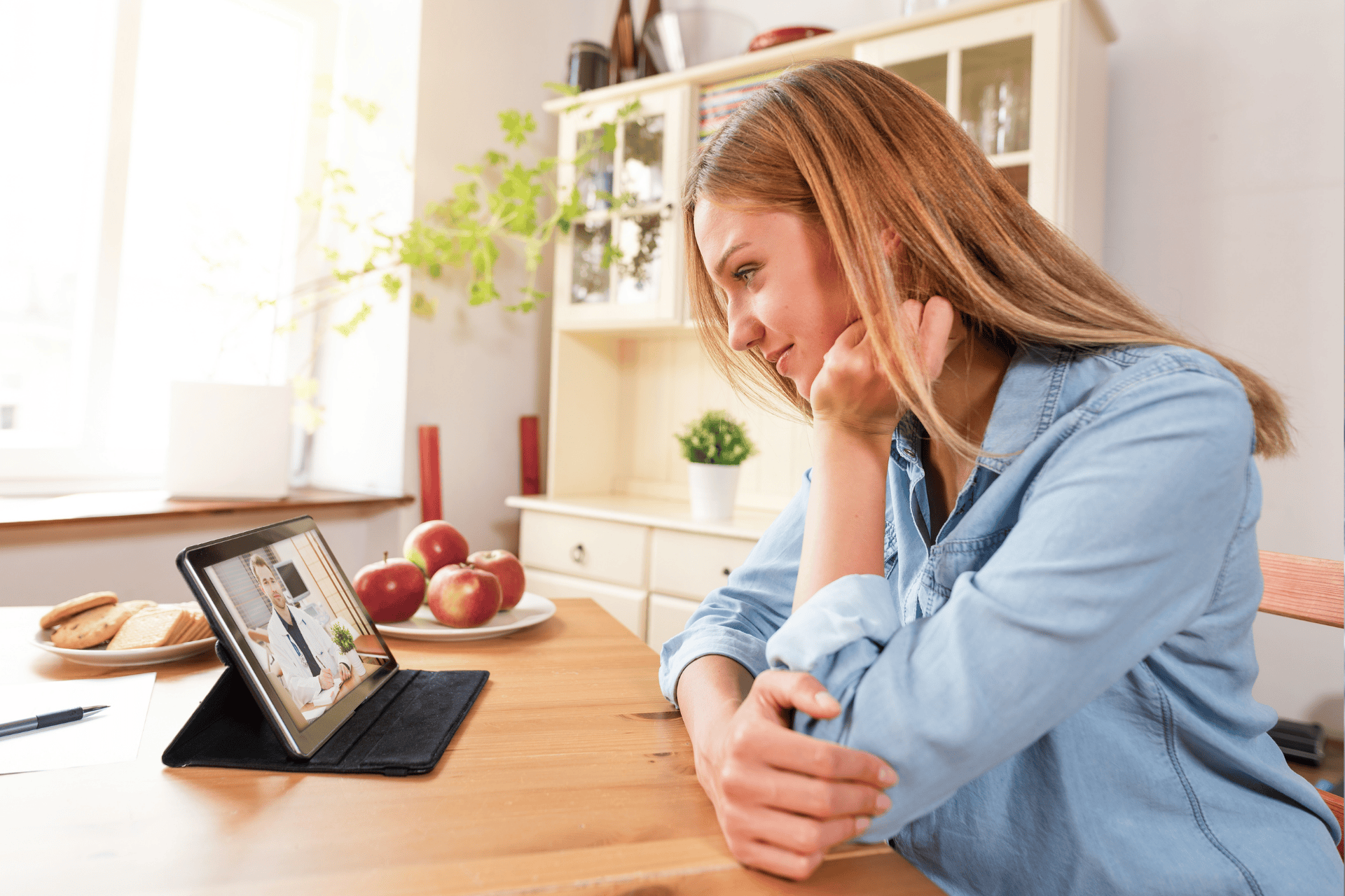 Woman having an online video consultation with a doctor using a tablet at home.