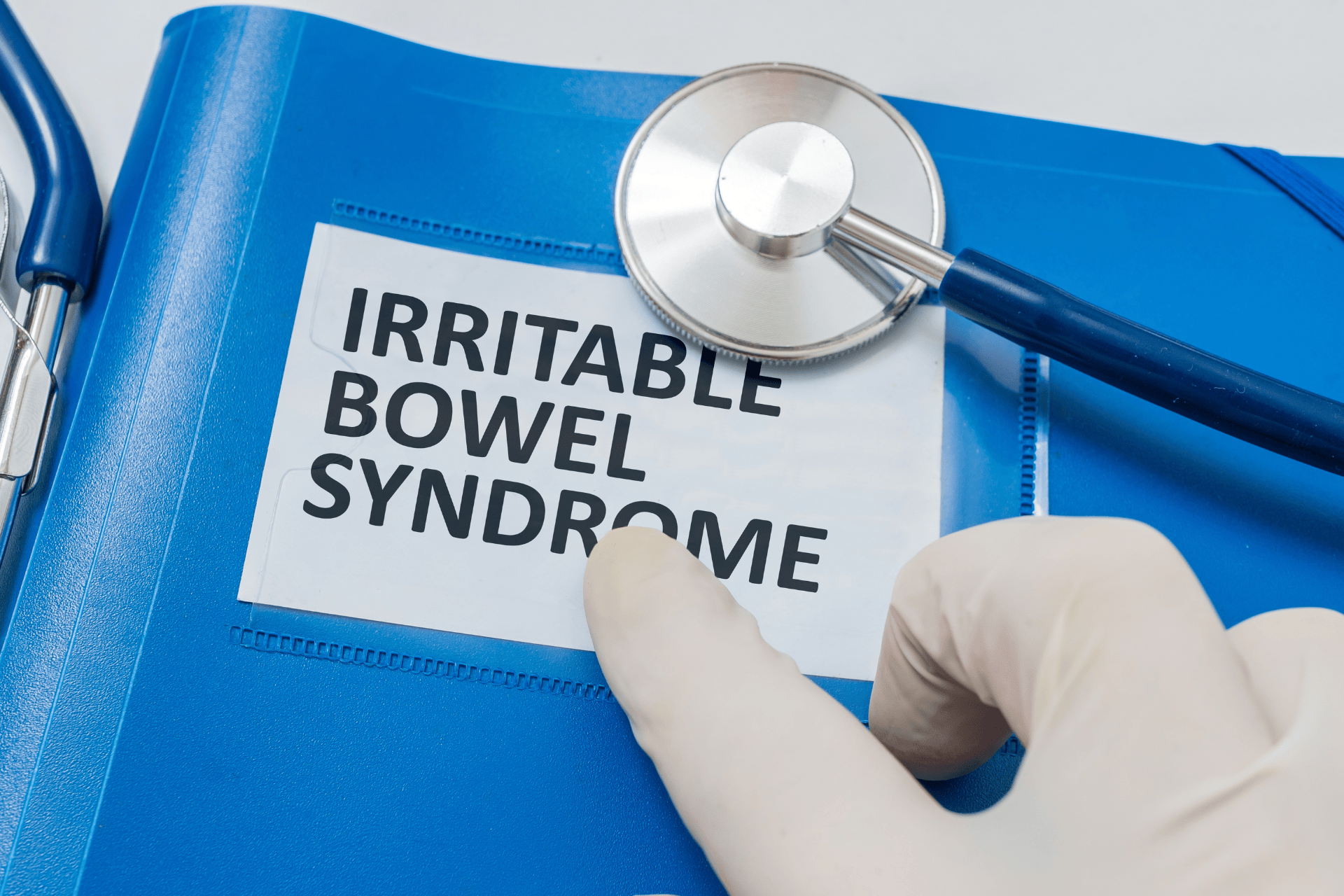 Gloved hand pointing to a folder labeled Irritable Bowel Syndrome with a stethoscope beside it.