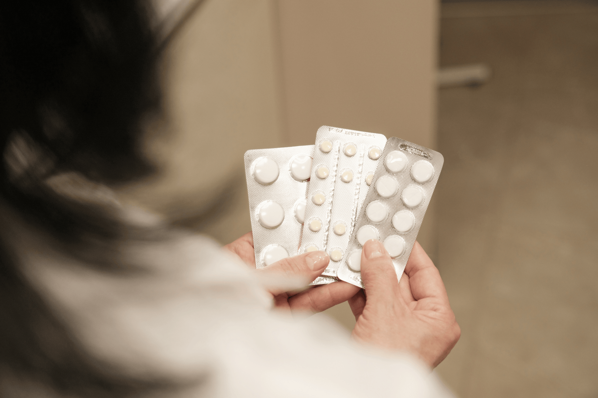 Person holding several blister packs of white tablets.