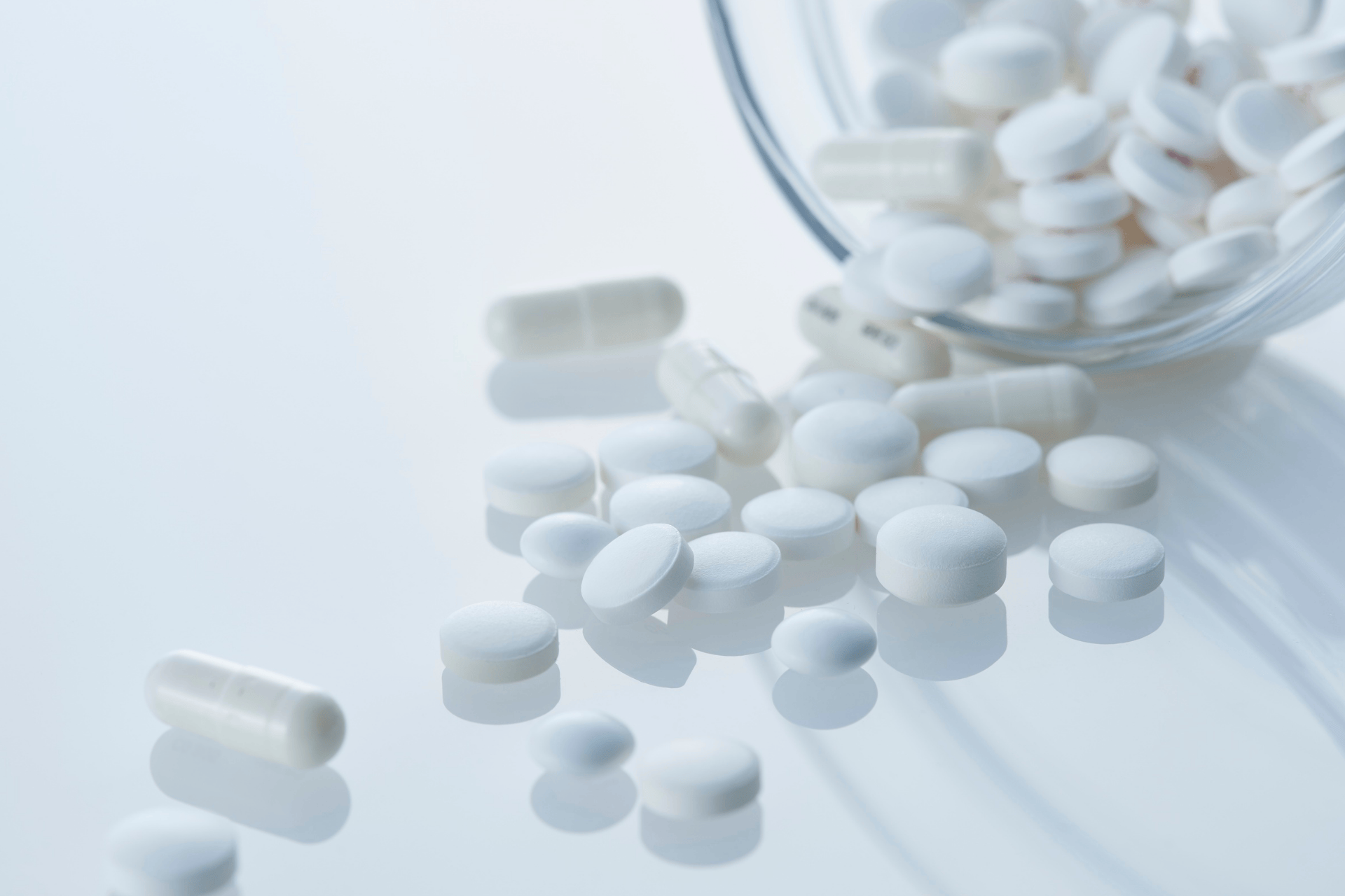 White round oval pills scattered on a surface beside a glass container.